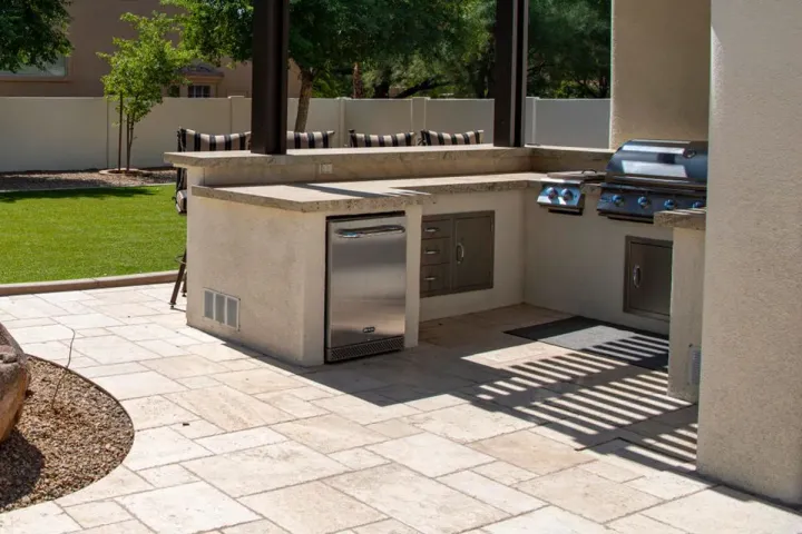 A built-in grill island with prep counters, drawers, and stainless appliances on a travertine patio
