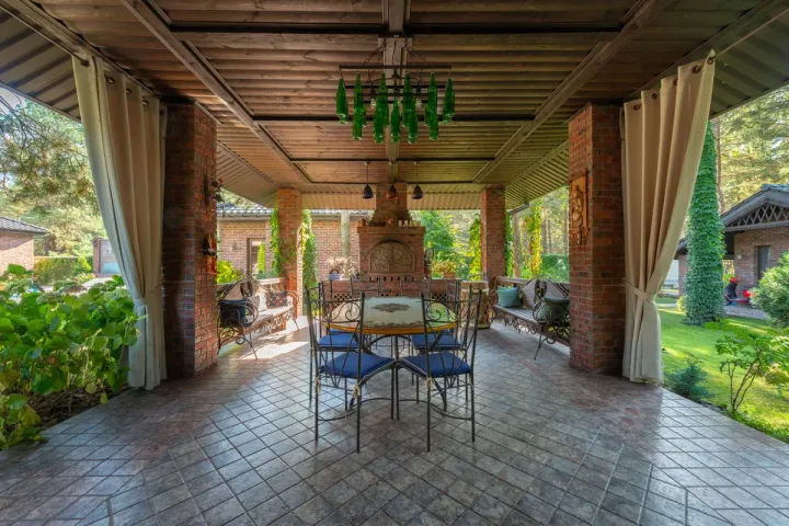 A covered outdoor dining room with brick columns, a masonry oven, and a paver floor