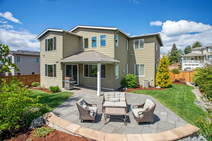 A paver patio with a curved contrasting border and wicker lounge seating in a landscaped backyard